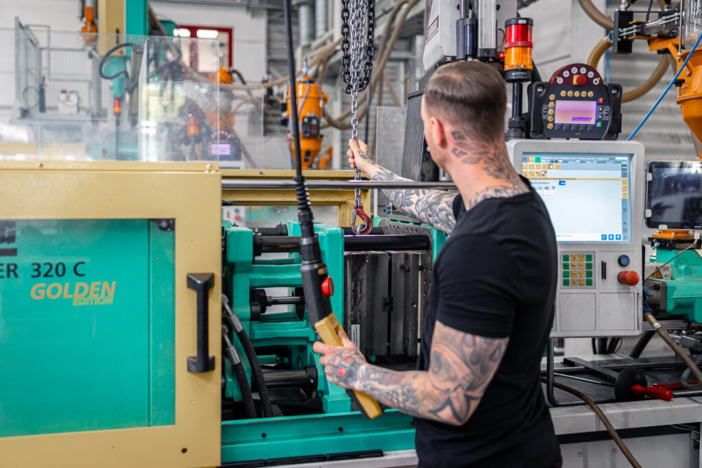 Ein Mitarbeiter mit Tattoos bedient eine Spritzgussmaschine für Kunststoff im Werkzeugbau bei Schröder und Heidler.