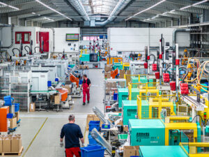Eine belebte Produktionshalle zeigt Maschinen für Kunststoff-Spritzguss und Arbeiter von Schröder und Heidler in Aktion.