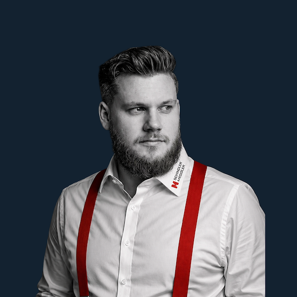 Ein Mann mit Bart und roten Hosenträgern posiert selbstbewusst vor einem blauen Hintergrund für Schröder und Heidler | © Schröder und Heidler.